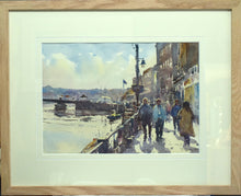 Load image into Gallery viewer, 9.5 x 13.5 inch watercolour, looking into the sunlight, with a bridge over the river on the left, building on the right, with several people walking on the pavement beneath.  Shows single cream mount with groove cut out  on inner edge, and a plain Oak frame moulding.
