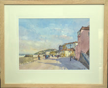 Load image into Gallery viewer, 10 x 13.75 inch watercolour of the promenade at Cromer, with many figures strolling along, the sea in the left distance, cliffs in the centre and buildings on the right. Shows the plain Oak frame with a cream, grrooved single mount.
