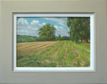 Load image into Gallery viewer, 10.5 x 17 inch oil painting of the field at the edge of the village, looking towards Wing, with large trees on the right, and a single Oak tree just left of centre, with the ruts of the stubble field taking the eye into the picture. Also shows the plain grey/beige frame with a white painted inner slip.

