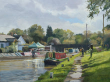 Load image into Gallery viewer, A 9 x 12 inch oil painting of narrowboats on the canal at Hillmorton near Rugby, looking into the sunlight, a footbridge in the middle distance, puddles on the towpath on the right, with two fellow artists painting.
