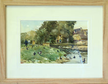 Load image into Gallery viewer, 6.5 x 10 inch watercolour of the River Welland by a footbridge on Stamford Meadows, with stone buildings on the right, mature trees above the bridge, many figures milling about and lots of ducks on the gras and in the water. Also shows the frame with a plain Oak moulding and an ivory mount.
