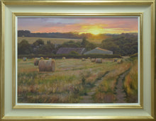 Load image into Gallery viewer, 20 x 28 inch oil painting of the golden setting sun on a high horizon, hedgerows in the middle and far distance, and two large barns, with many round bales on a stubble field in the foreground. Shows cream/beige hand-finished gessoed frame, with gold metal-leafed inner and outer edges, with off-white inner slip.
