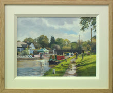 Load image into Gallery viewer, A 9 x 12 inch oil painting of narrowboats on the canal at Hillmorton near Rugby, looking into the sunlight, a footbridge in the middle distance, puddles on the towpath on the right, with two fellow artists painting, also showing cream inner frame with plain Oak outer frame
