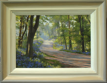 Load image into Gallery viewer, 10 x 14 inch oil painting of the path through Barnsdale Wood, looking into the sunlight, trees appearing dark, with a sparkle of lit vegetation and foliage, with lots of Bluebells abounding. showing hand-finished grey outer to beige and off-white inner frame
