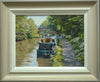 9 x 12 inch oil painting of narrowboats on the Oxford Canal at Braunston, near Daventry., with a hump-back bridge in the middle distance, trees on the far bank, and overhanging trees on the right where the towpath takes the eye alongside the boats. Also shows frame with off-white inner slip gradating to beige and grey outer moulding.