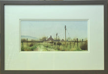 Load image into Gallery viewer, A letterbox-shaped 6 x 13 inch watercolour of a farmhouse and some barns, painted on a damp day in Pembrokeshire, with a track taking the eye from bottom left of centre round to the right , with some bushes, fenceposts and telegraph poles simply described. Photo shows the ivory double-mount with warm grey frame moulding.
