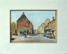 Load image into Gallery viewer, Print of a watercolour painting of High Steet East, Uppingham, Iconic view of the shops on the right, and what was a flower shop occupying the single, ancient building on the left, with several figures so deftly described, strong shadows across the road. Set in a single ivory mount, with a thin gold inner wooden slip.
