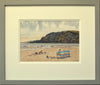 Small watercolour, 7 x 10 inches, of Pentewan Beach in Cornwall, with the dark headland and colourful windbreak in the mid-ground, with many people having fun on the sand and in the surf, showing the double-mount and grey outer frame moulding.